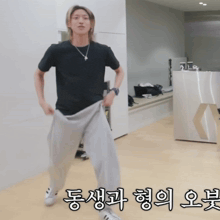 a man in a black t-shirt and grey sweatpants is standing in a room with korean writing on the floor