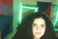 a woman with curly hair is smiling in front of a sign that says happy halloween .