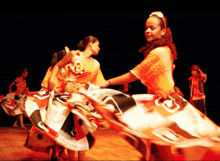 a woman in a yellow top is dancing with another woman in a red and white dress