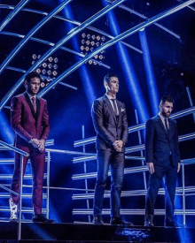 three men in suits are standing on a stage in front of a blue light