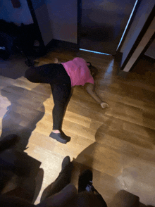 a woman in a pink shirt is laying on the floor in a dark room