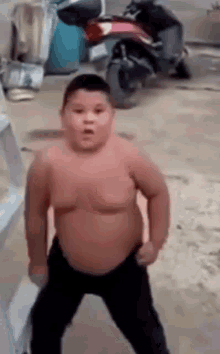 a fat boy without a shirt is standing in front of a motorcycle .