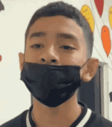 a young man wearing a black face mask looks at the camera