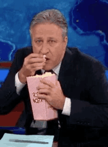 a man in a suit and tie is eating popcorn from a box