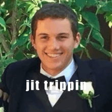 a man in a tuxedo and bow tie is smiling in front of a bush with the words jit trippin above him .