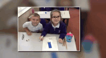 a boy and girl are sitting at a desk in a classroom .