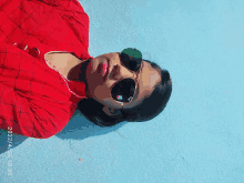 a woman wearing sunglasses and a red shirt is laying on the ground