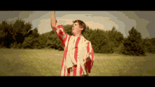 a man in a red and white striped shirt is standing in a field with his arms in the air