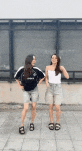 two women are standing next to each other on a sidewalk and dancing .
