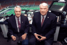 two men sit in a booth in front of a football field that says nfl