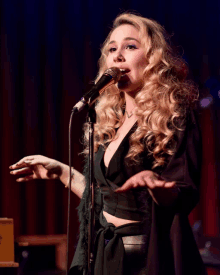 a blonde woman singing into a microphone with her hands outstretched