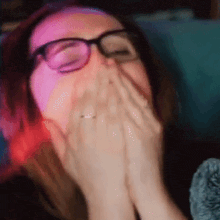 a woman wearing glasses is covering her face with her hands