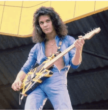 a man in a blue jumpsuit is holding a guitar with a yellow and black strap