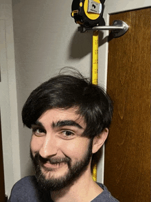 a man with a beard is measuring his height with a tape measure hanging on a door