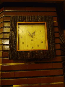 a wooden clock on a brick wall shows the time as almost 5:00