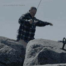 a man in a plaid shirt is standing on a rock in front of a la guanmba film festival poster