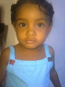 a little girl wearing a blue tank top with flowers on the sleeves