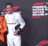 a man in a white suit is holding a trophy in front of a sign that says formula 1 qatar grand prix .