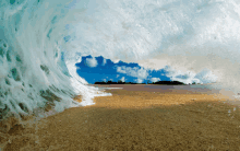 a wave breaks on a sandy beach with a blue sky in the background