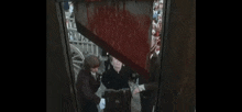 a man and a woman are standing next to each other in front of a large container filled with blood .