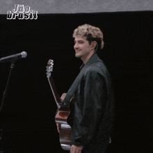 a man in a black jacket is holding a guitar in front of a black background that says " joo brasil "