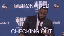 a man in a suit and tie sits at a table in front of a wall that says nba finals