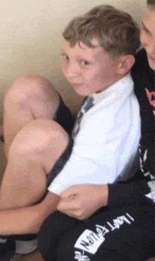 a young boy in a white shirt and tie is sitting next to another boy .