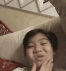 a young boy is laying on a bed with his hands on his face and making a funny face .