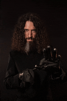 a man with long curly hair and a beard is wearing a black coat and gloves