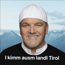 a man wearing a white hat is smiling in front of mountains and the words i kimm ausm landl tirol on the bottom