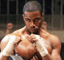 a shirtless boxer with boxing gloves on his hands is standing in a boxing ring .
