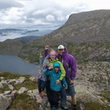 a family is posing for a picture on top of a mountain with a lake in the background .