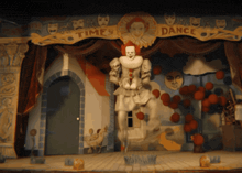 a clown on a stage in front of a banner that says time to dance