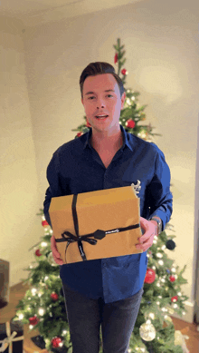 a man in front of a christmas tree is holding a gift box that says ' abercrombie & fitch ' on it