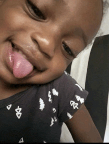 a little girl sticking her tongue out and wearing a blue shirt with trees on it