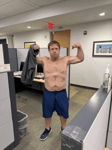 a shirtless man flexes his muscles in a cubicle