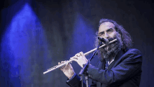 a man with long hair and a beard is playing a flute in front of a microphone