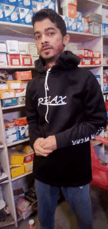 a man wearing a black relax hoodie stands in front of a shelf full of boxes