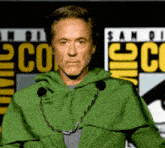 a man in a green cape stands in front of a comic con sign