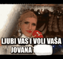 a woman is holding a microphone in front of a sign that says ljubi vasi i voli vasa jovana 1