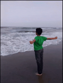 a young boy in a green shirt is standing on the beach with his arms outstretched