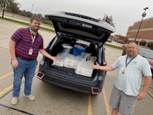 two men are standing next to a car with the trunk open