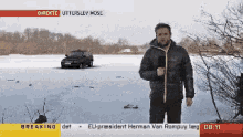 a man is standing in front of a frozen lake with a car in the background and breaking at the top