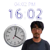 a man with glasses stands next to a clock that says 16:02
