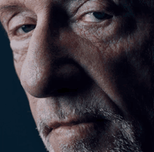 a close up of an older man 's face with a beard and blue eyes