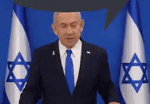 a man in a suit and tie is standing in front of a flag with a star of david on it .