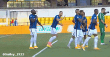 a group of soccer players are celebrating a goal on a field with an ad for smiley 1932 in the background