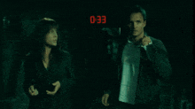 a man and a woman are standing in front of a digital clock that reads 0:28