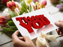 a person holding a thank you card with flowers in the background