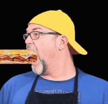 a man wearing a yellow hat and glasses is eating a sandwich